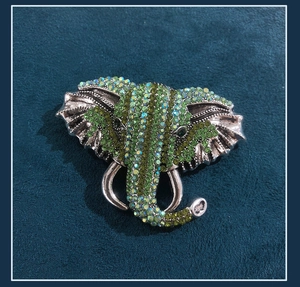 Close-up of vintage elephant brooch featuring green crystals on antique silver metal