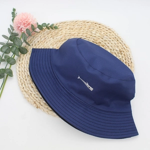 Deep navy cotton bucket hat with small silver fish embroidery on a natural straw mat