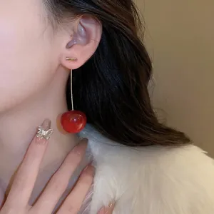 Elegant cherry drop earrings with red gloss finish and gold stems worn by a model