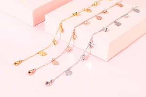 Three-color metal anklets with lucky clover and bell pendants on pink background