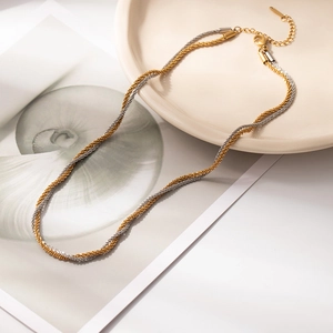 Elegant gold and silver twisted chain necklace with beaded tassel on a ceramic plate