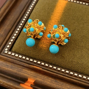 Gros plan de boucles d'oreilles boules dorées avec perles turquoise sur velours vert