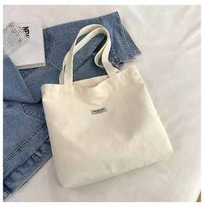 Flat lay of cream canvas tote bag with fashion label on soft white bed linen