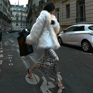 Look de rue : femme en manteau de fausse fourrure blanche et robe longue satinée léopard