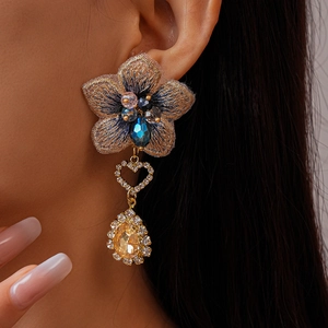 Gros plan sur boucle d'oreille fleur asymétrique avec broderie bleue et cristal goutte jaune