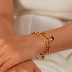 Detail of layered gold bracelets with black heart pendant and clear zircon accents