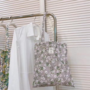 Dettaglio borsa tote in tela floreale con etichetta su sfondo camicia bianca