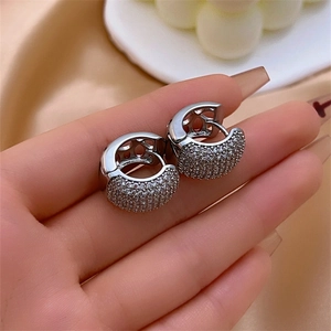 Elegant silver hoop earrings with white zircon crystals held against a satin fabric