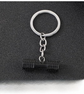 Close-up of a black dumbbell keychain for fitness fans on a dark textured surface