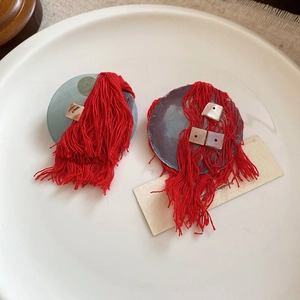 Artistic round earrings with vibrant red fabric tassels and square shell accents on a tray