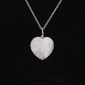 Macro view of silver wire tree of life wrapped around heart-shaped pink crystal necklace