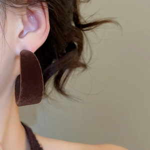 Gros plan d'une boucle d'oreille en velours marron foncé en forme de C sur un mannequin