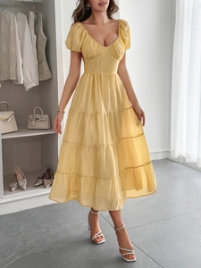 Dettaglio di un abito midi giallo con maniche a sbuffo, scollo a V e gonna a balze