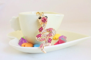Close-up of golden snake keychain with pink and white rhinestones on beige background