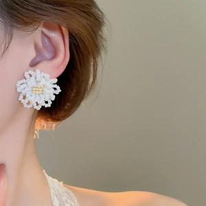 Close-up of a model wearing elegant beaded flower stud earrings with gold accents
