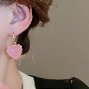 Close-up of model wearing sweet pink resin heart earrings with elegant gold frames