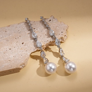 Macro detail of silver zircon earrings with elegant drop pearl on beige stone