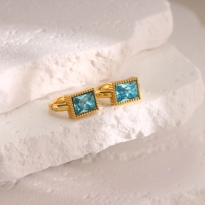 Macro shot of rectangular blue zircon earrings with gold beaded edges on white stone