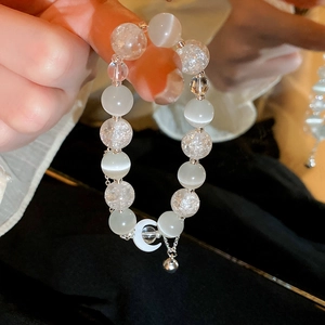 Close-up of cat eye stone bracelet with crescent moon charm and silver bell detail