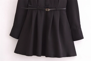 Detail of a black long-sleeve dress featuring a pleated waist and a slim belt with gold buckle