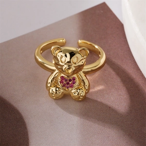 Detail of gold teddy bear ring featuring a pink heart gem on a textured background