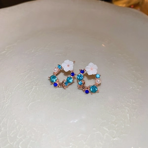Detail of rose gold flower earrings with blue rhinestones and white pearls on ceramic