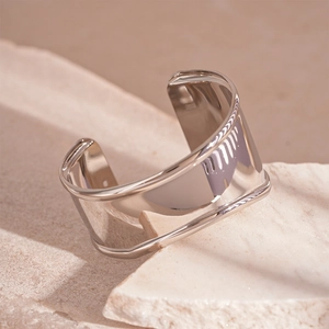 Detailed close-up of glossy silver wide metal cuff bracelet on stone texture base