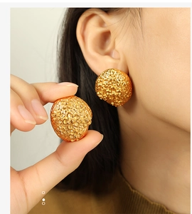 Detail of 18k gold plated ball earrings with intricate floral relief pattern on texture