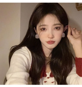 Close-up of elegant square zircon earrings with fabric texture worn by a model in soft light