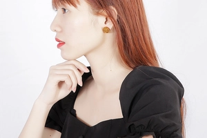 Detail of round golden stud earrings with embossed anchor pattern on a female model