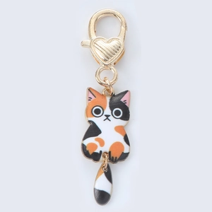 Detail of calico cat enamel charm with golden heart-shaped lobster clasp for bags