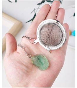Detail of 304 stainless steel tea infuser with raw green crystal stone on hand