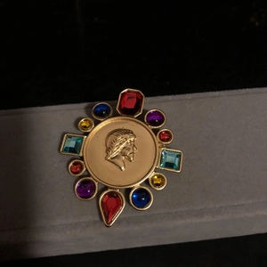 Vintage gold brooch with colorful gemstones and antique coin relief on black background