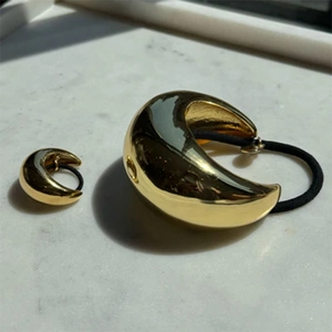Golden moon-shaped metal hair ties in two sizes on white marble surface