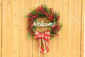 Detail of Christmas wreath with red berries, wooden Welcome sign, and plaid bow