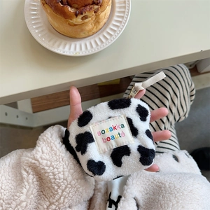 Detail of cow print plush mini makeup bag held in hand showing compact storage size