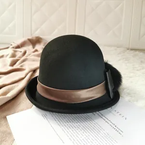 Detail of wool cloche hat with brown ribbon, leather bow, and fluffy pompom ornament