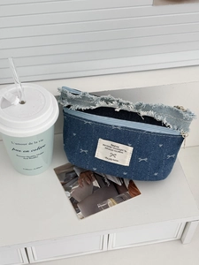 Detailed view of the denim makeup bag showing raw fringe edges and white woven label