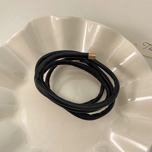 Detail of a minimalist black faux leather hair tie with gold metal tips on a ceramic plate