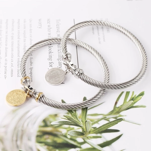 Detailed close-up of stainless steel cable bracelets with gold Saint Benedict pendant charms