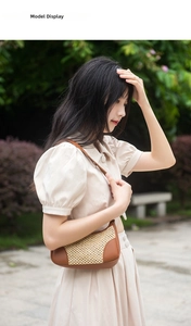 Detail view of woven straw underarm bag with brown leather trim on beige summer dress