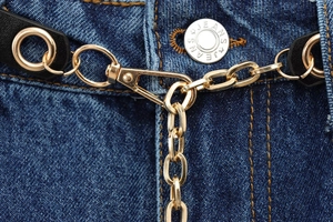 Dettaglio della cintura a catena in metallo dorato con anelli su jeans in denim blu