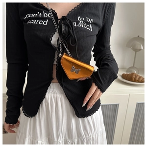 Détail du mini sac bandoulière orange métallisé avec fermoir papillon sur cardigan noir