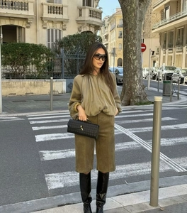 Street style shot of a woman in khaki long sleeve top and Bermuda shorts with black boots