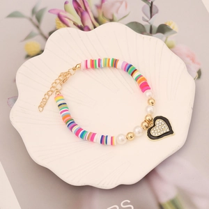 Colorful polymer clay heart bracelet with pearls and gold accents on a white dish
