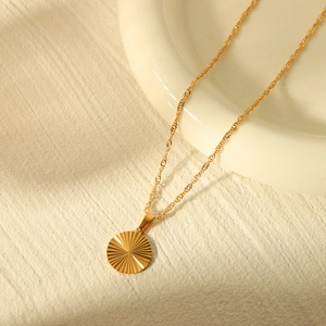 Detail view of a gold circular heart pendant with sunburst texture on a twisted rope chain