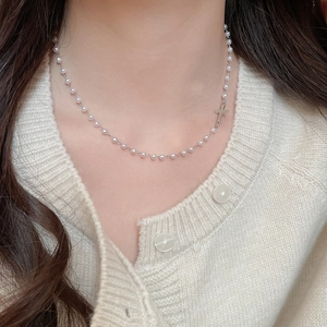 Detail of elegant cross pendant pearl necklace on cream knit sweater for women