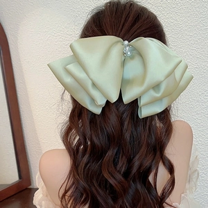 Large light green satin bow hair clip with pearl detail shown on brown wavy hair
