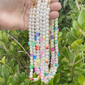 Detail of pearl necklace with colorful charms like lemon slices and stars on a gold clasp