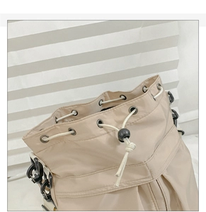 Detail of beige nylon drawstring bucket bag with metal eyelets and adjustable toggle